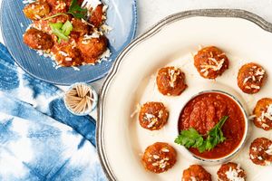 Meatballs in marinara sauce arrange in a circular pattern on a serving dish next to toothpicks and a smaller bowl of meatballs and parmesan.