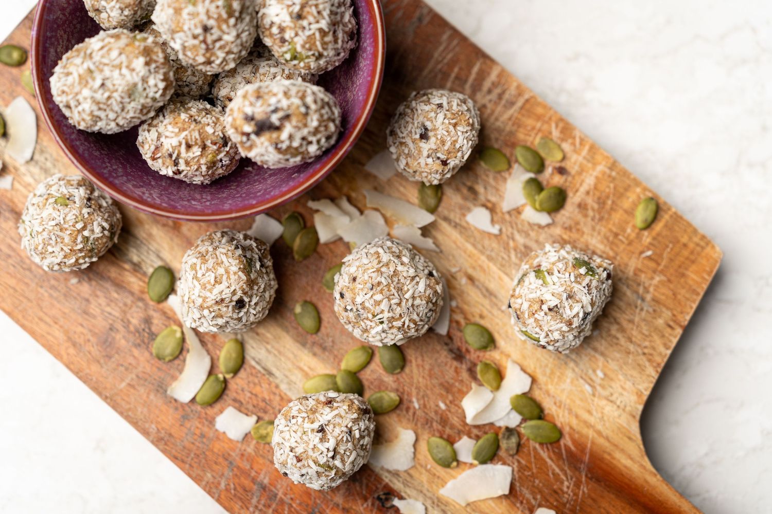 Small balls made of nut butter and other seeds on top of a wooden cutting board.