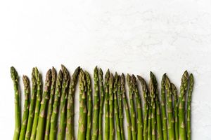 Fresh green asparagus spears neatly lined up on a white marble surface, showcasing their vibrant color and texture.