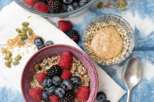 A bowl of fresh mixed berries on top of a chia and hemp seed type of pudding. Seeds scattered about on top of a tie dye blue napkin.