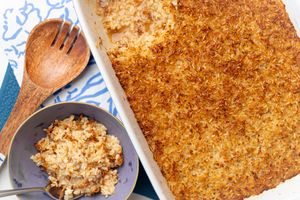 A baked rice dish piping hot in a serving dish straight from the oven. Next to it a small bowl with a serving of the browned rice dished out