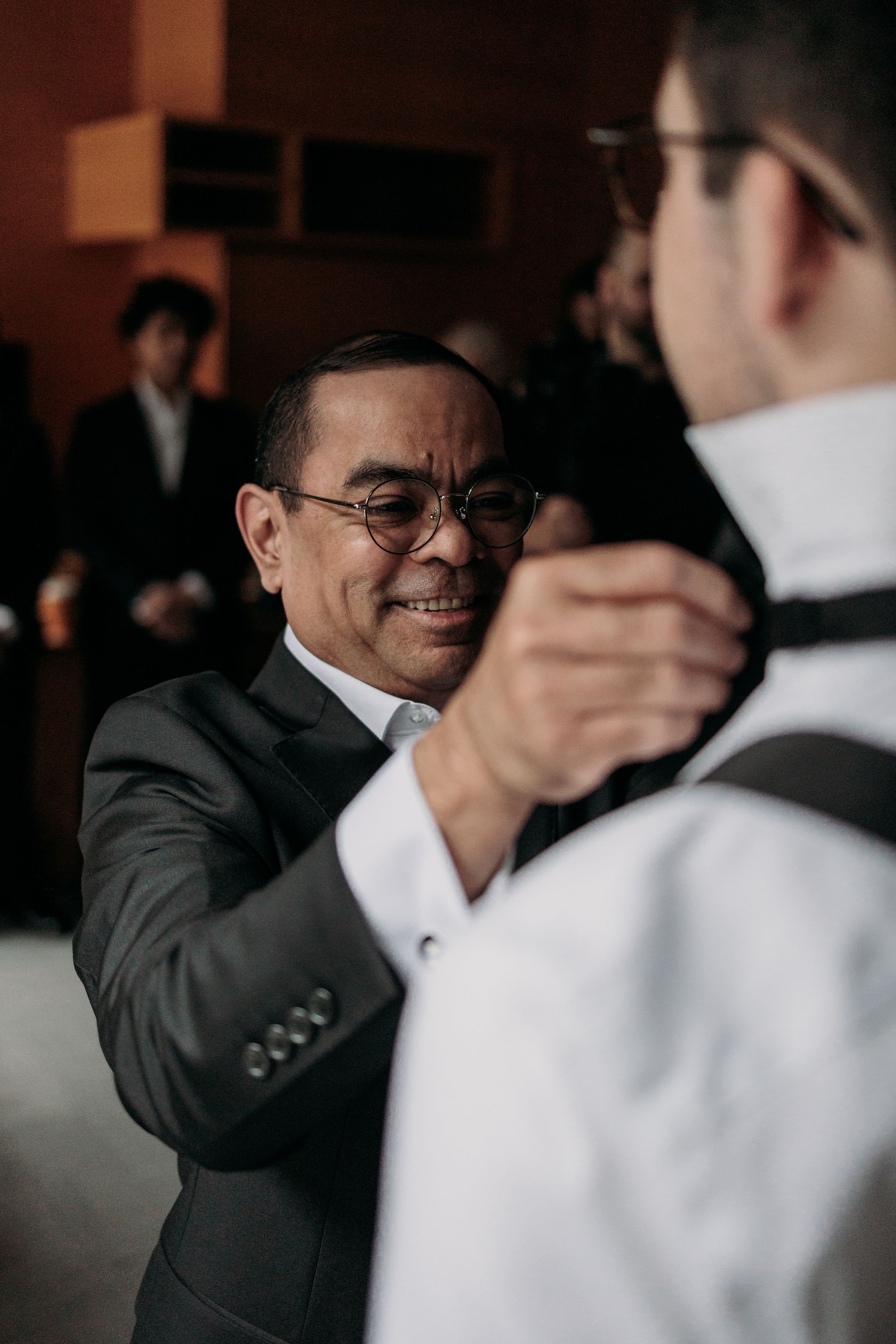Two men in suits share an emotional greeting or handshake during what appears to be a formal event.