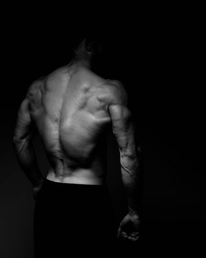 Black and white photo of a muscular man's back showing defined muscles against a dark background.