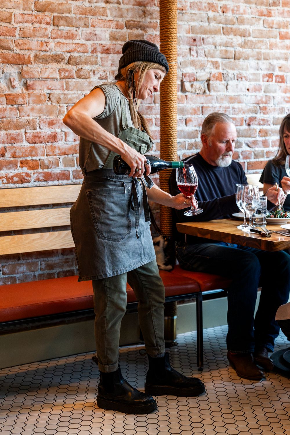 Server in an apron pouring wine for diners in a rustic restaurant setting.