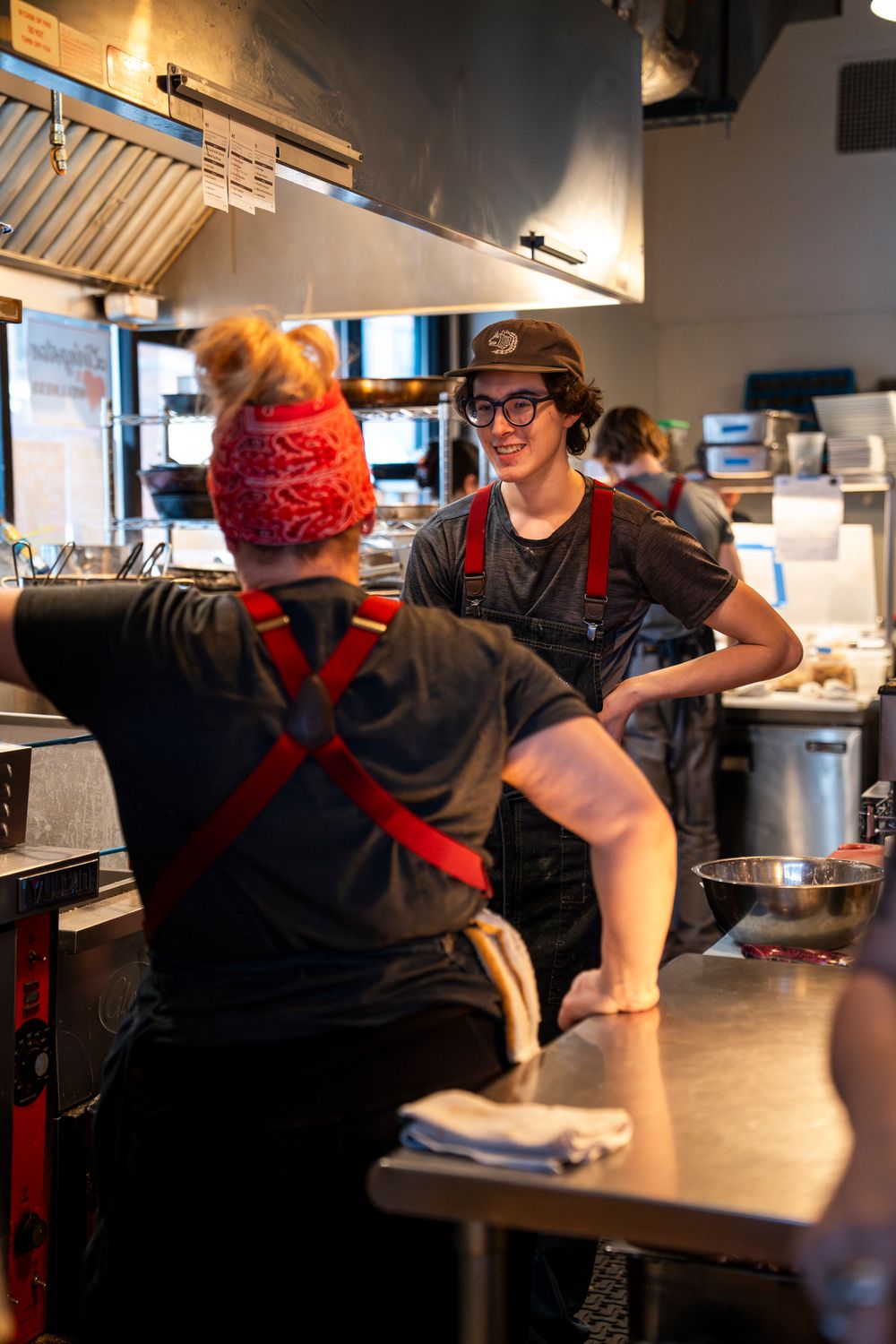 Kitchen staff interacting in a commercial restaurant kitchen with stainless steel equipment.