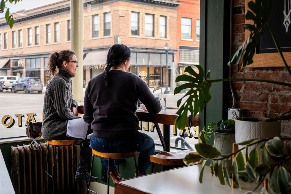 Customers enjoying coffee at a window seat in an urban cafe setting.