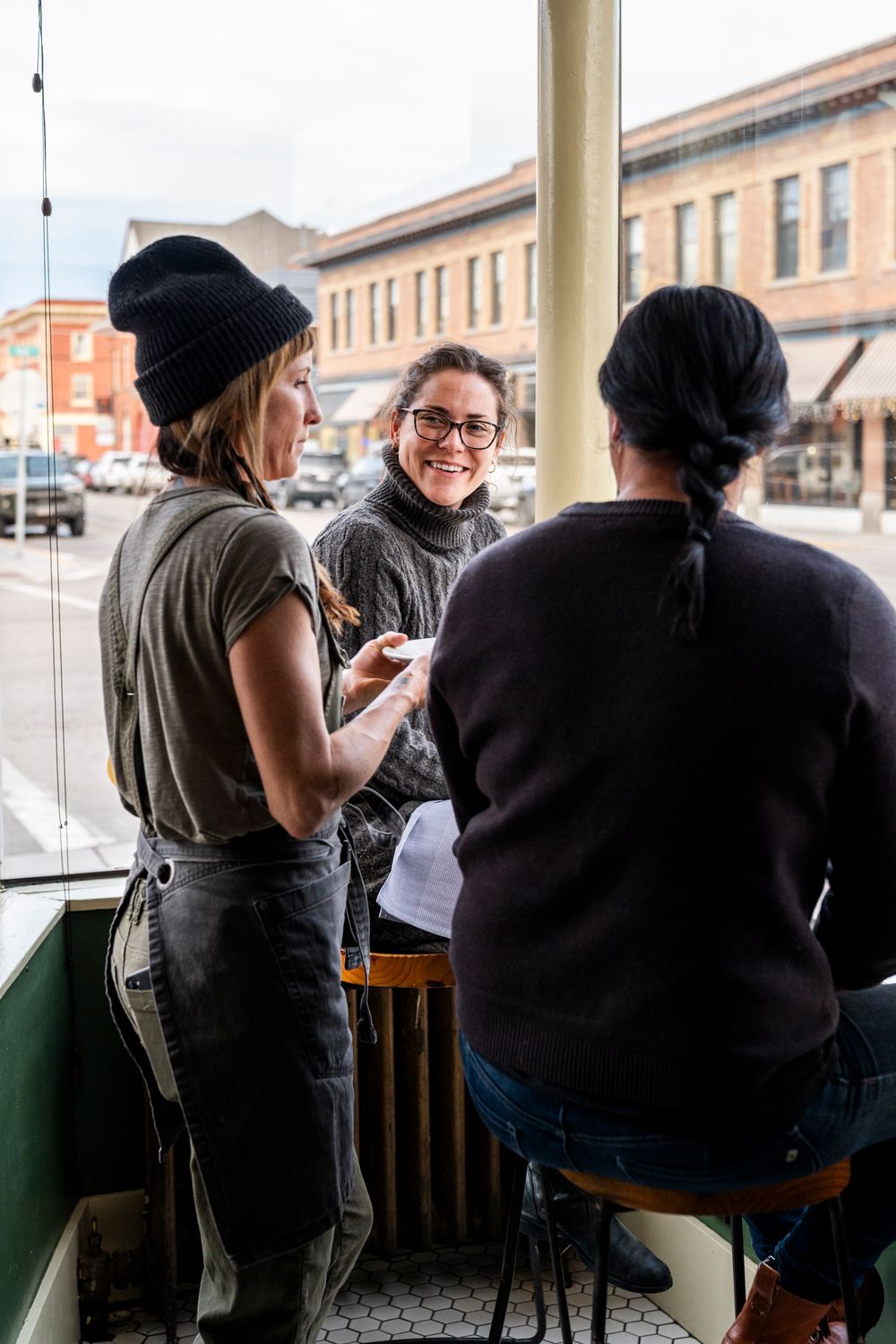Restaurant staff having a casual conversation in a window seating area.