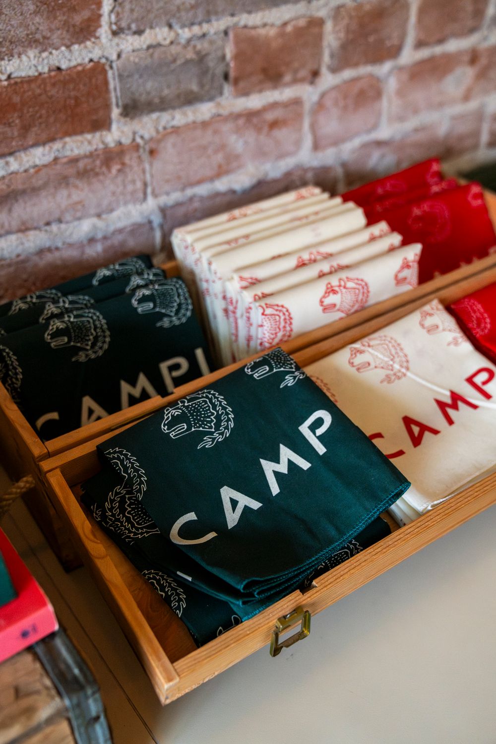 Branded CAMP merchandise displayed on wooden shelves against exposed brick wall.