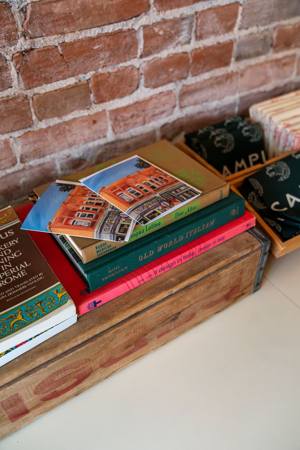 Books and retail merchandise arranged on wooden display shelf against brick wall.