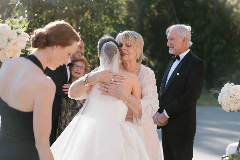 Emotional outdoor wedding ceremony scene with embracing guests and formal attire in sunlit garden setting.