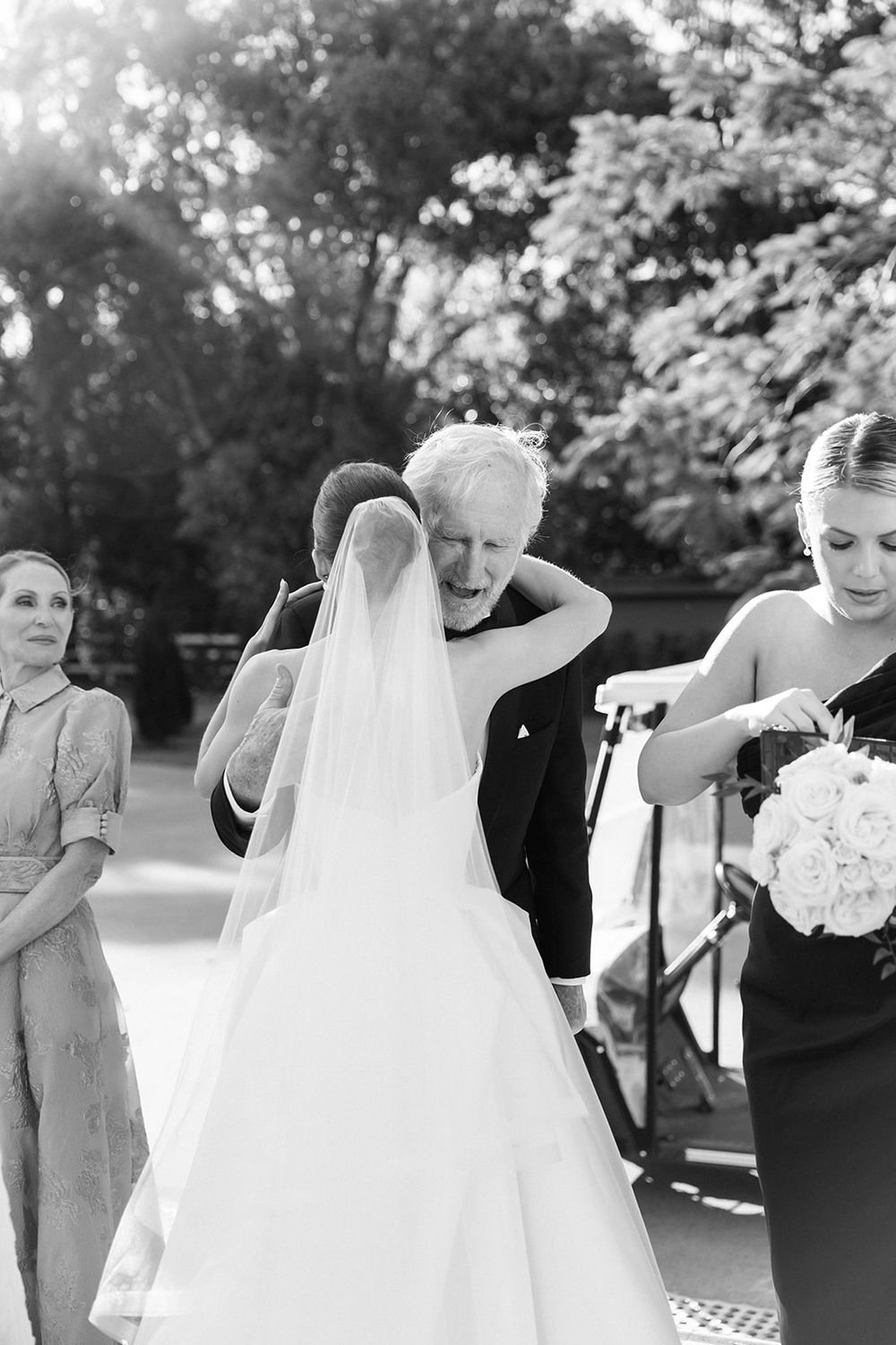 Wedding party gathers outdoors on a sunny day for portrait photos in black and white.