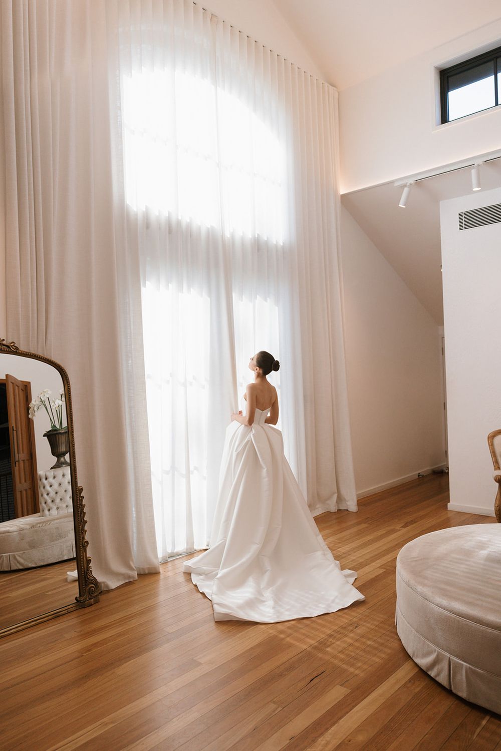 A sequence of minimalist wedding dress photos in a bright white room with hardwood floors and flowing curtains.