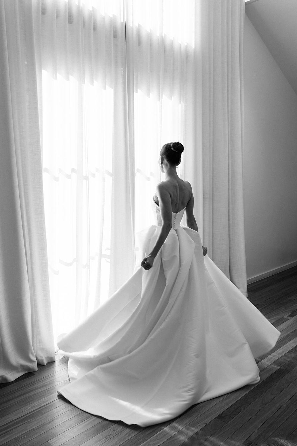 A sequence of four black and white photos showing the flowing train of a white wedding dress on a dark hardwood floor.