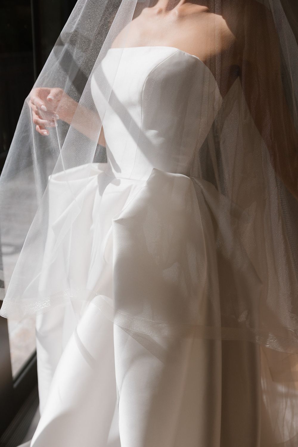 Close-up view of white bridal gown details showing elegant draping and flowing veil material.