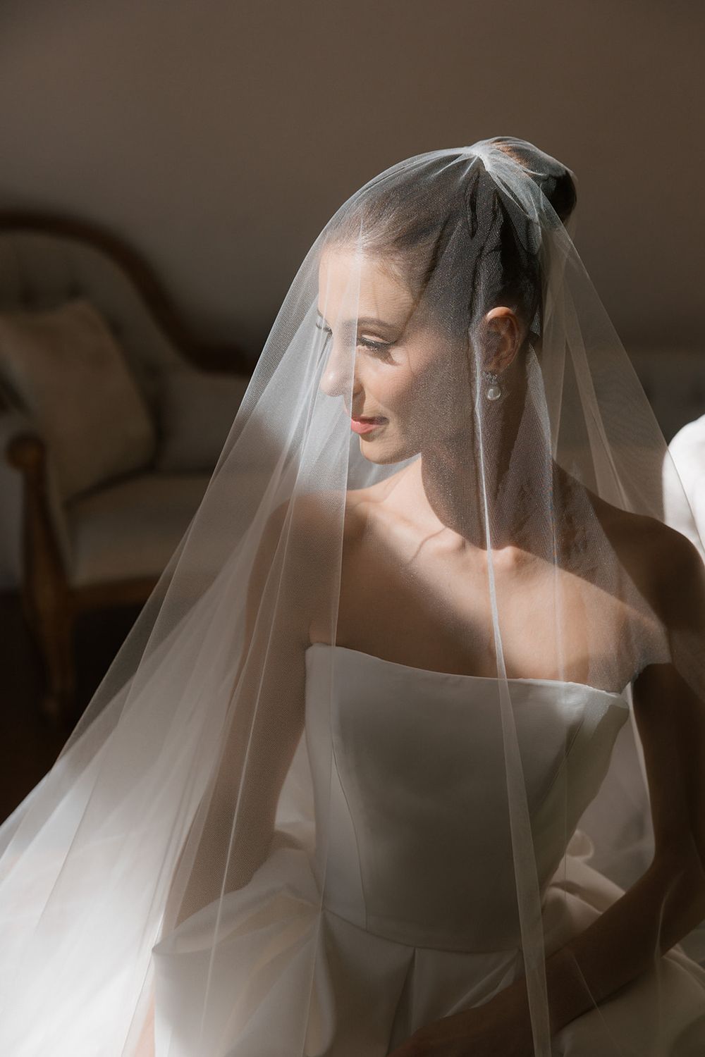 A bride in soft lighting wears a delicate white veil that flows around her in an ethereal bridal portrait series.