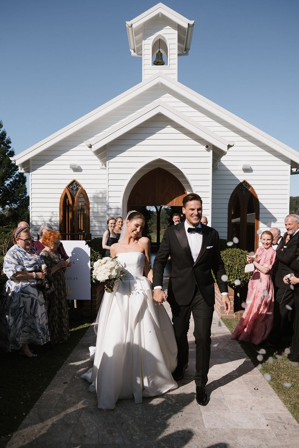 A wedding series showing a couple exiting a white wooden chapel after their ceremony while guests celebrate.