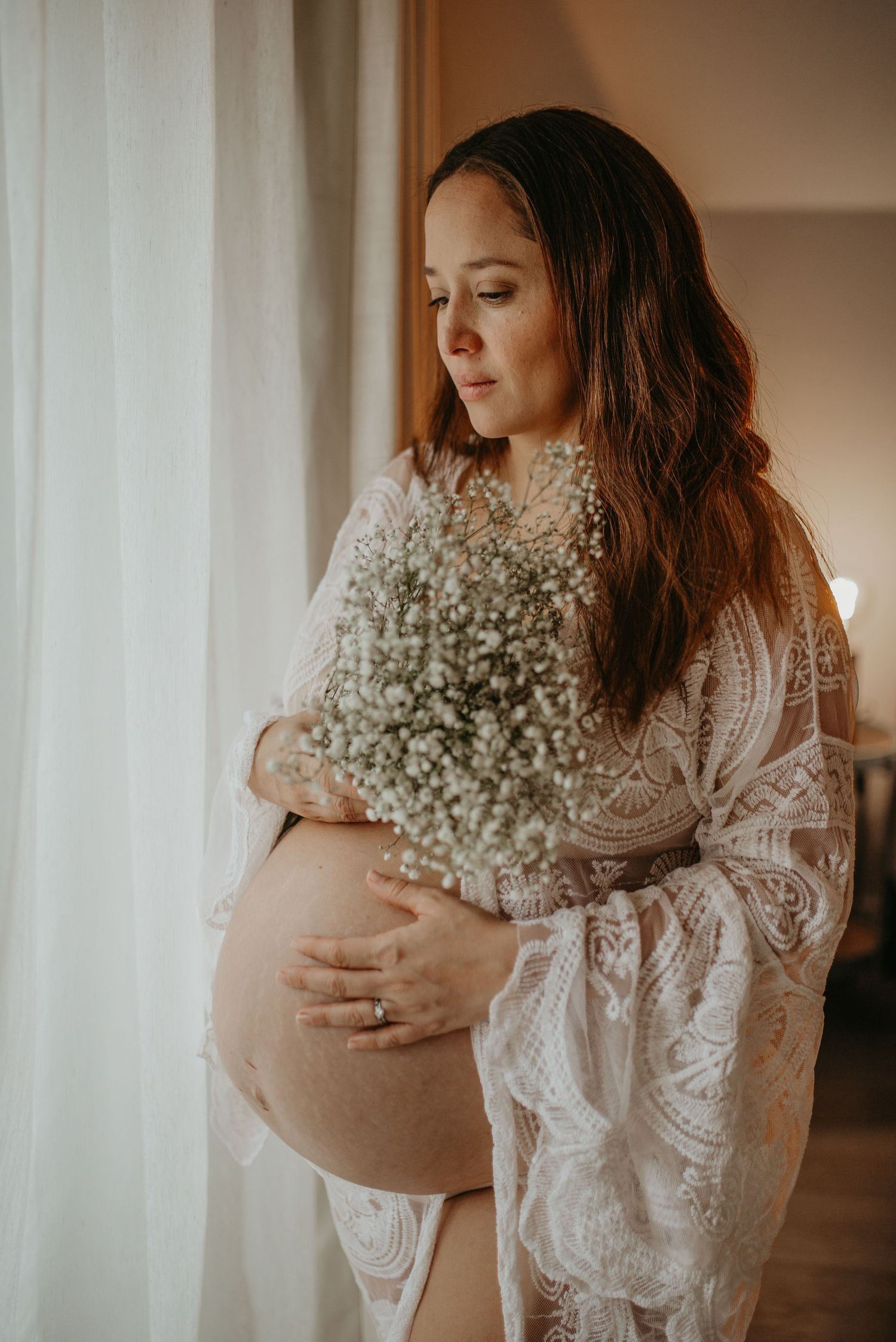 A romantic maternity photoshoot features a person in a flowing beige dress against a neutral backdrop. photography in South-East london