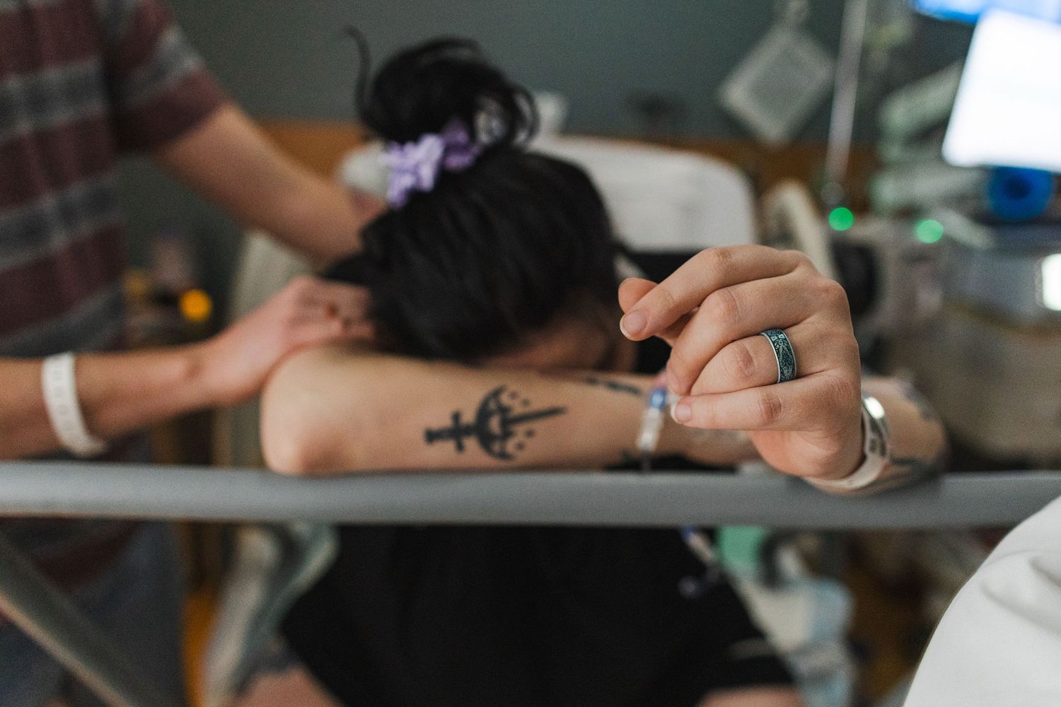 Someone rests their head on a desk while getting a small tattoo applied to their arm.