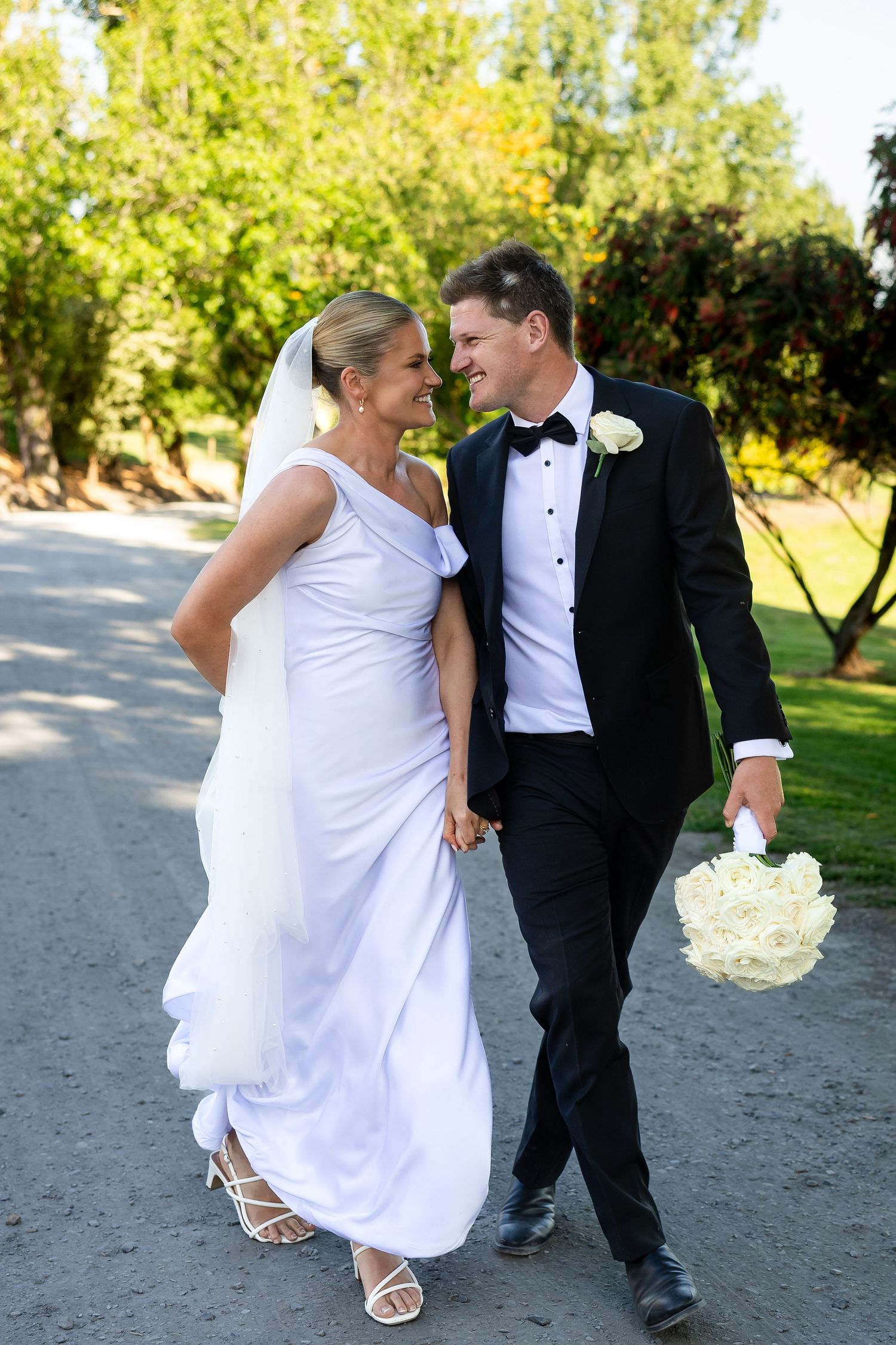 A couple in wedding attire celebrates by popping champagne in a golden field at sunset.