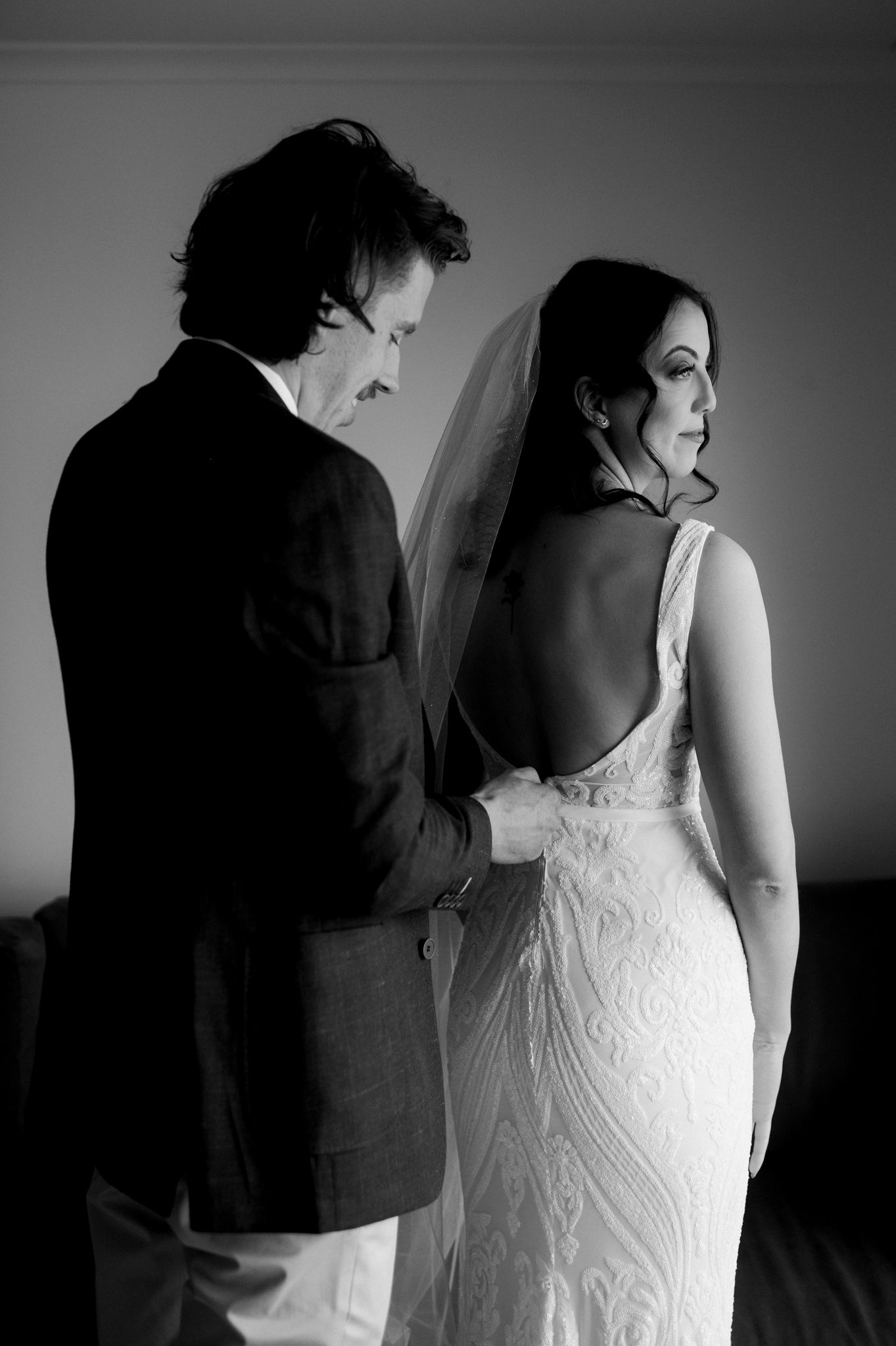 A dramatic black and white shot shows a couple on their wedding day, with the bride in a fitted lace gown and the groom adjusting it.