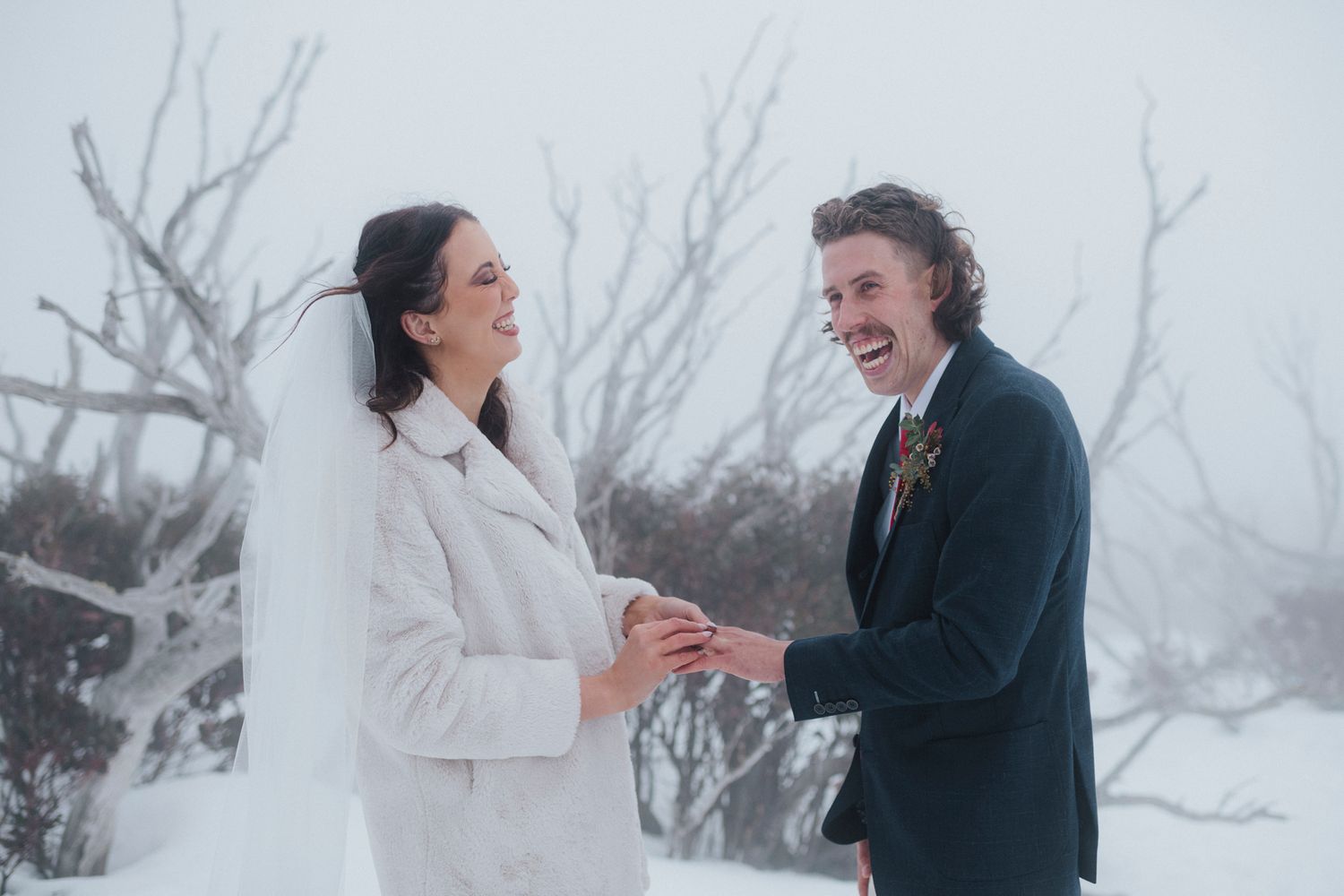 Joyful couple laughs together during winter photoshoot in the snow.
