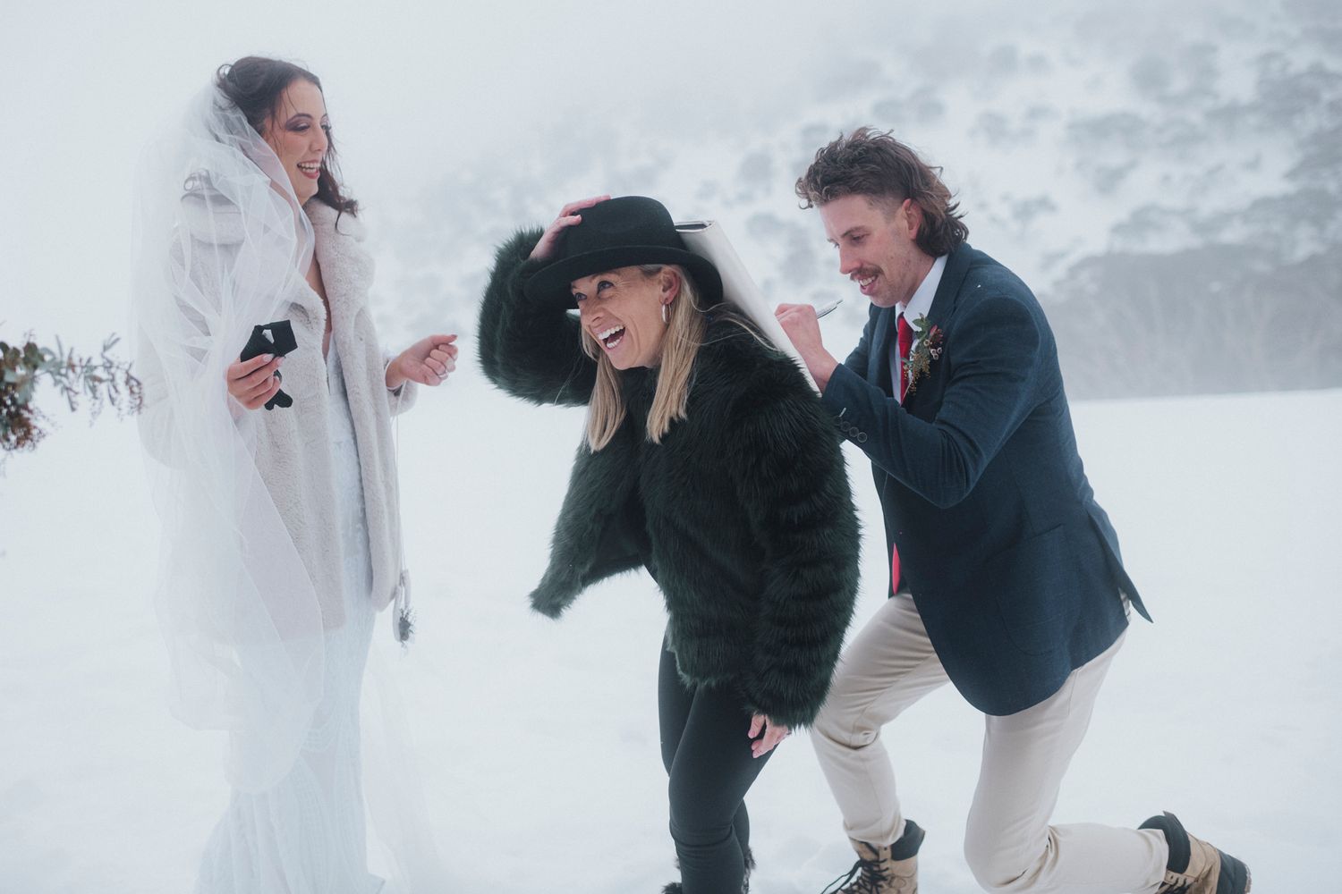 Wedding couple playing in fresh snow during winter wedding photoshoot with photographer.