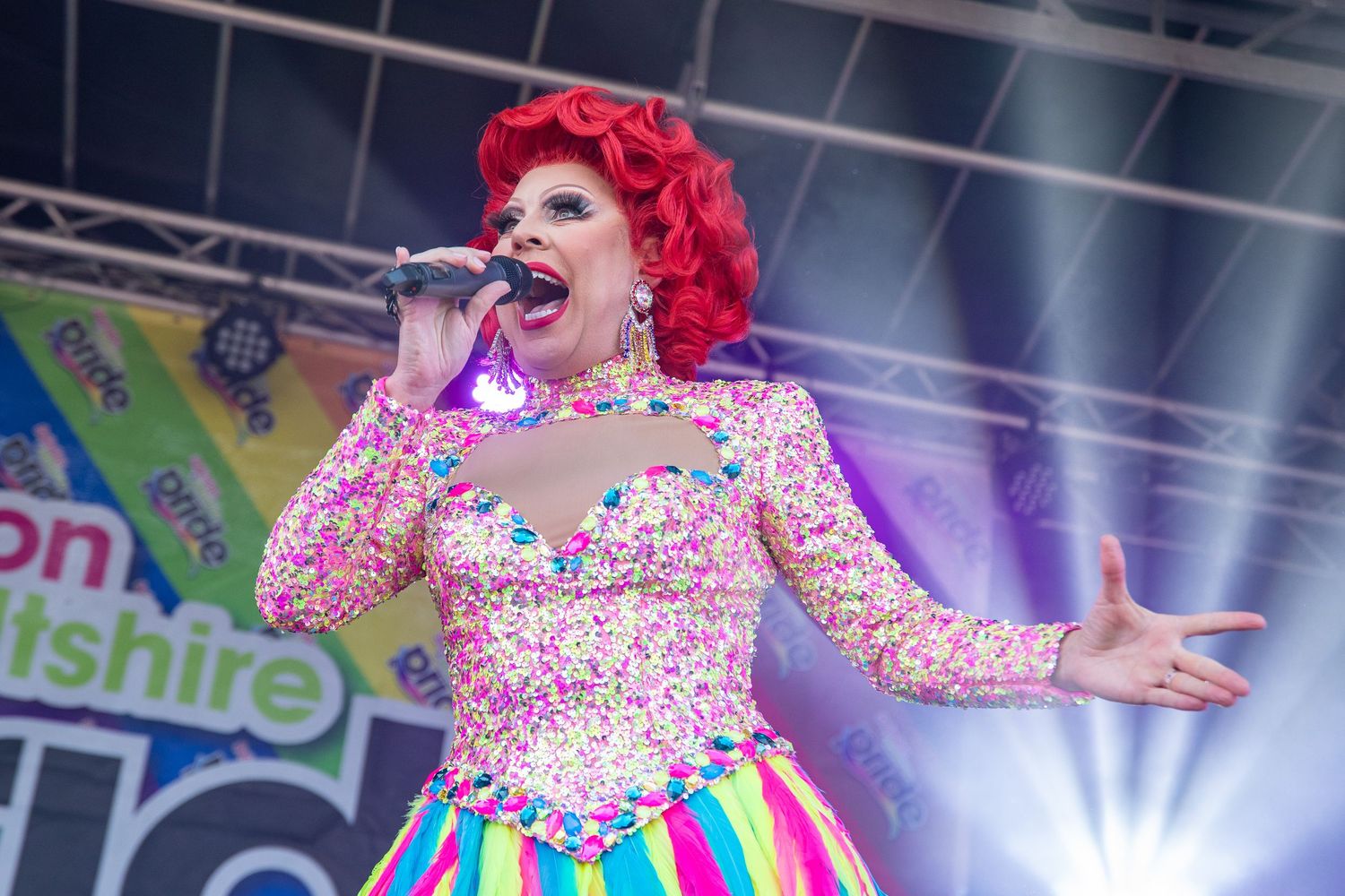 Entertainer in a colorful rainbow dress performing on stage with dramatic lighting.