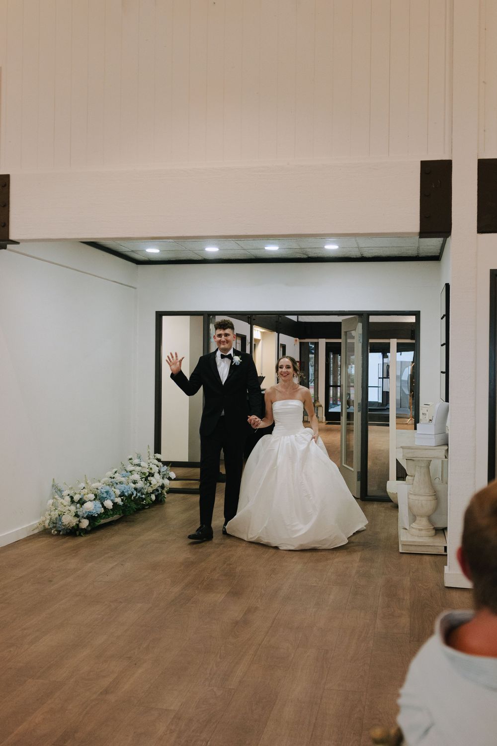 A couple makes their grand entrance at a wedding reception in a modern venue with white walls and hardwood floors.