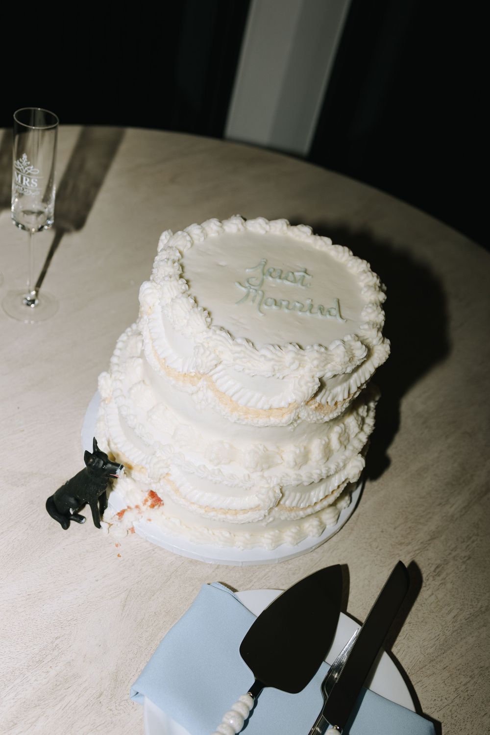 A classic white wedding cake with delicate piping details sits on a table with serving utensils nearby.
