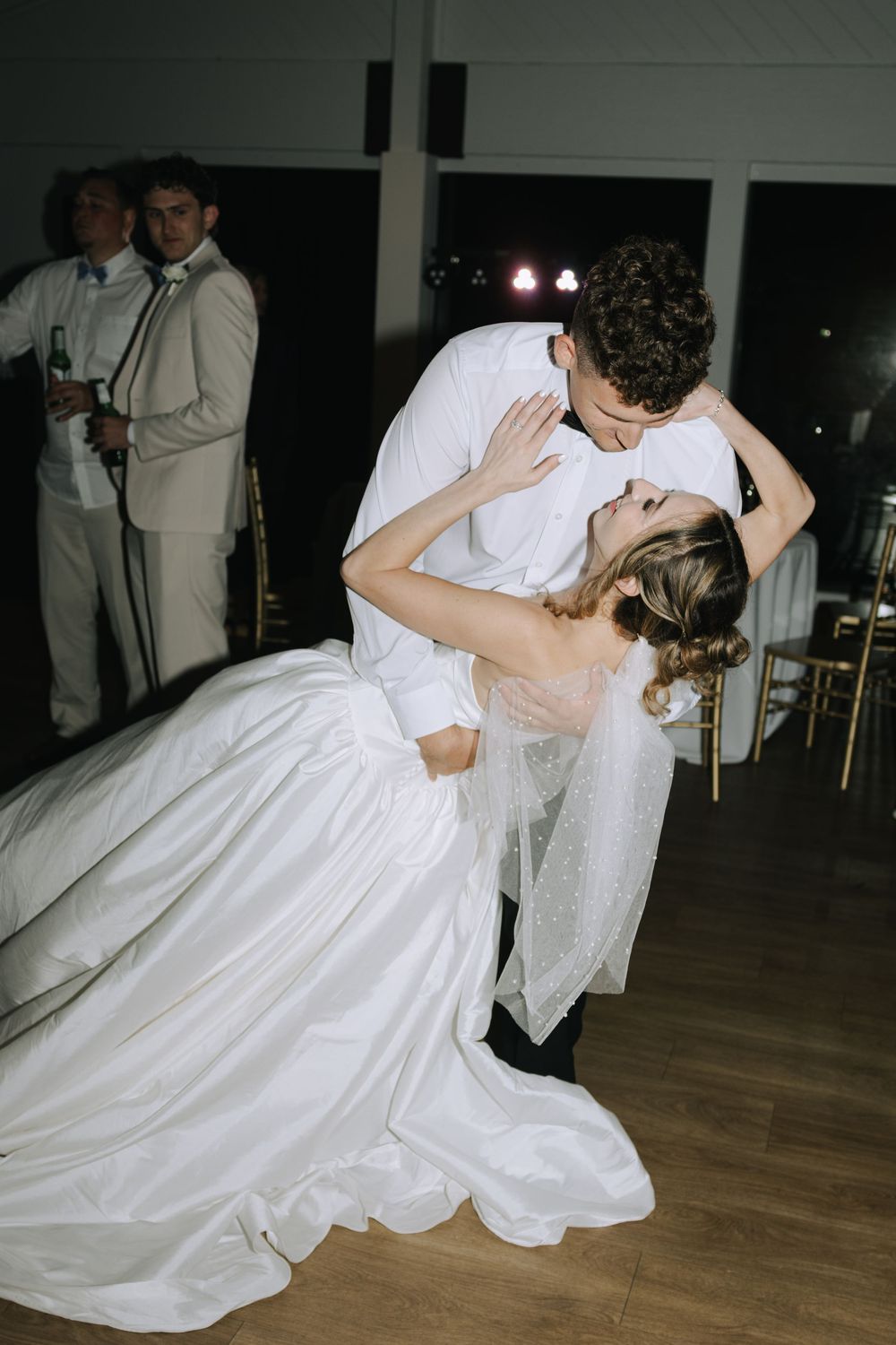 A romantic dip on the dance floor showcases a flowing white wedding gown during a reception.