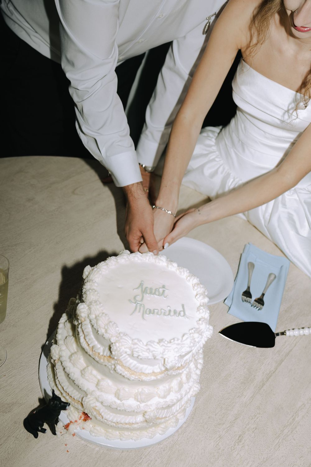 White wedding cake being decorated with delicate piping and frosting details on a table.