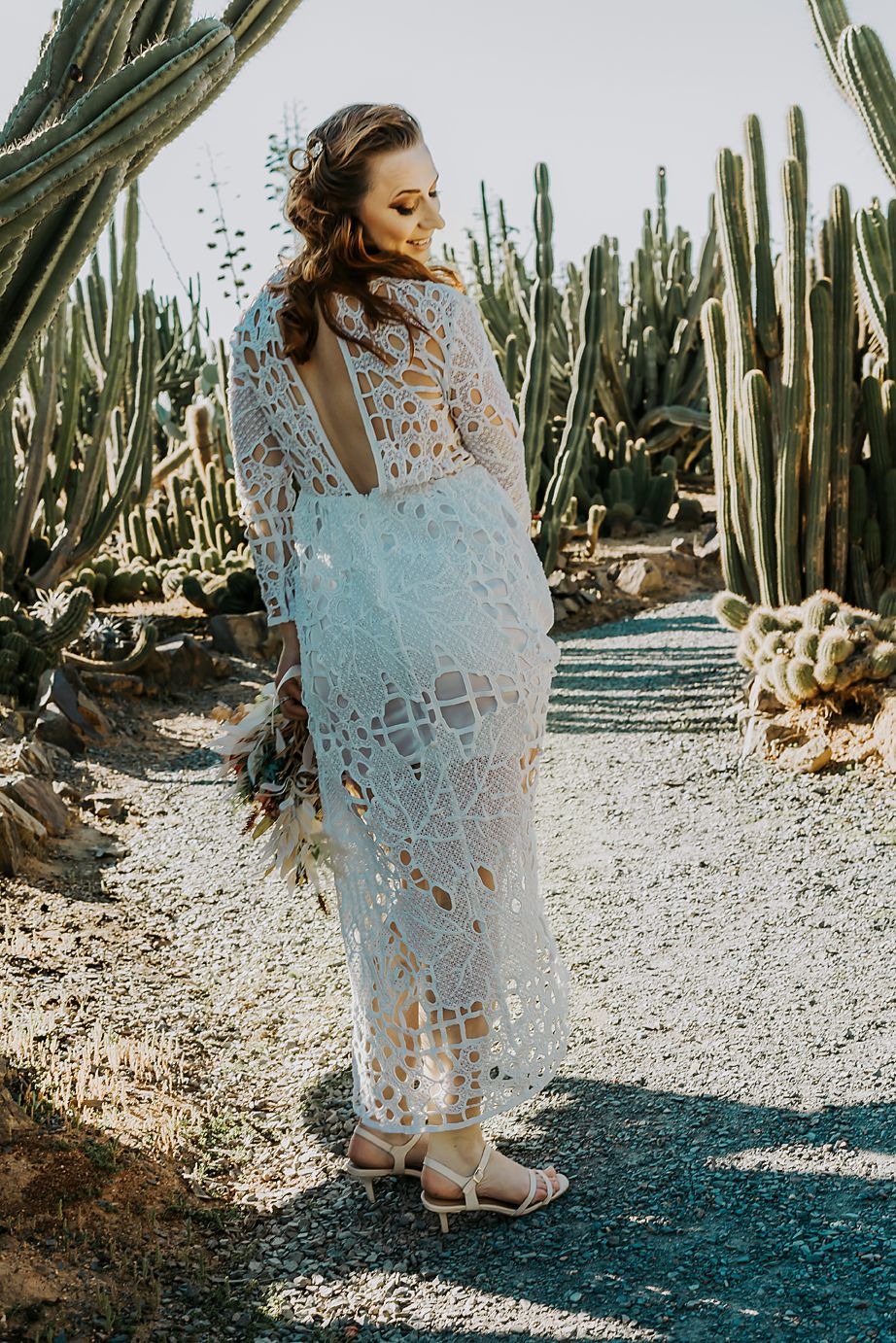 A white lace dress with sheer details photographed in a desert garden setting with tall cacti and natural sunlight.