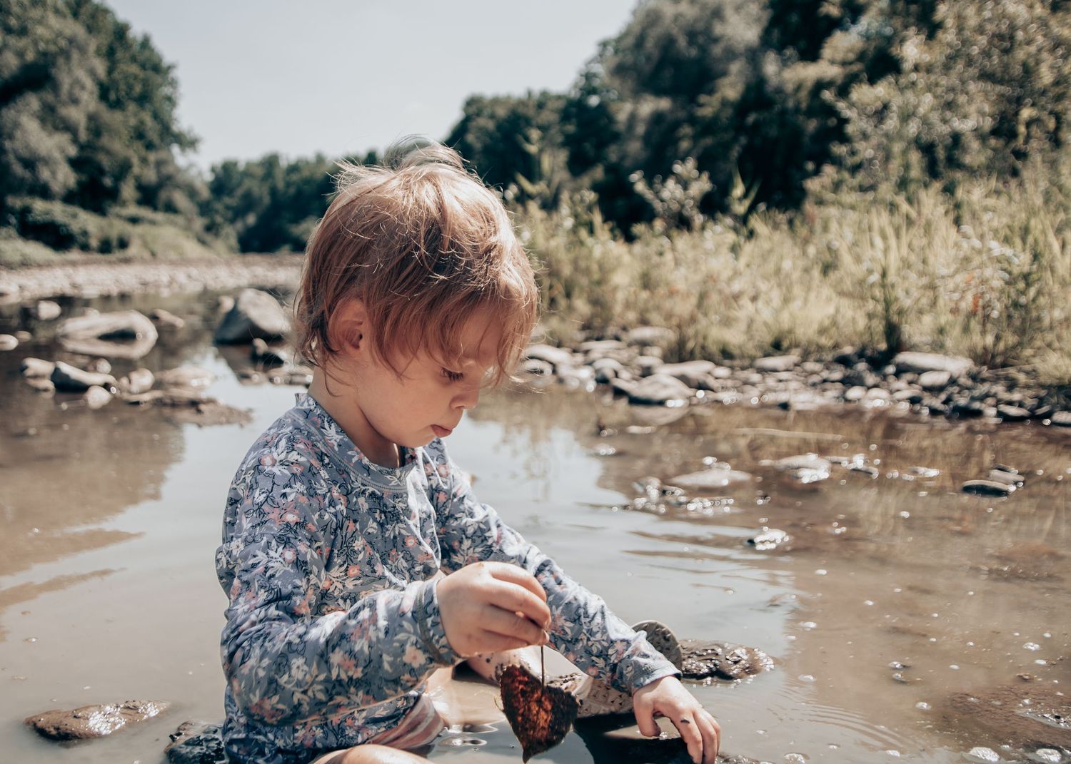 Young child exploring and playing in shallow water by a rocky shore.