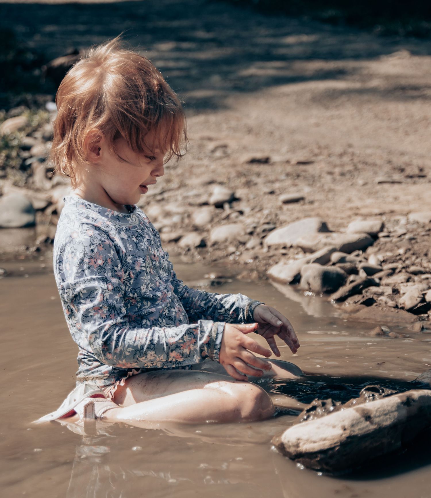Child exploring and playing with rocks in shallow muddy water.