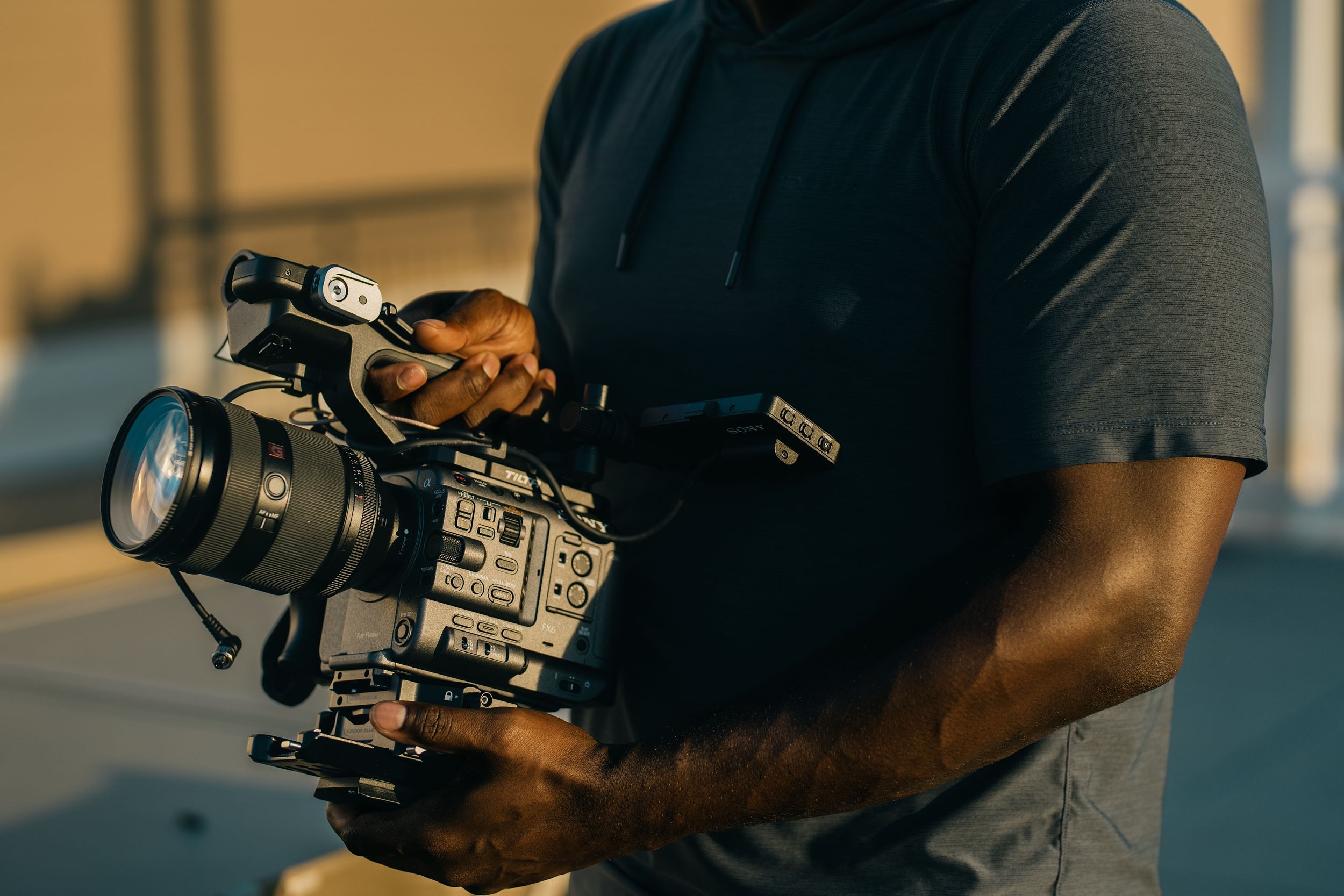 Professional videographer operates camera equipment while filming outdoors during golden hour lighting.