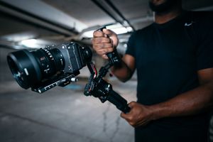 Close-up shot of hands holding professional camera equipment with stabilizer gimbal in dim lighting.