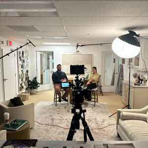 Professional photography studio setup with lighting equipment, furniture, and various camera angles in a modern office space.