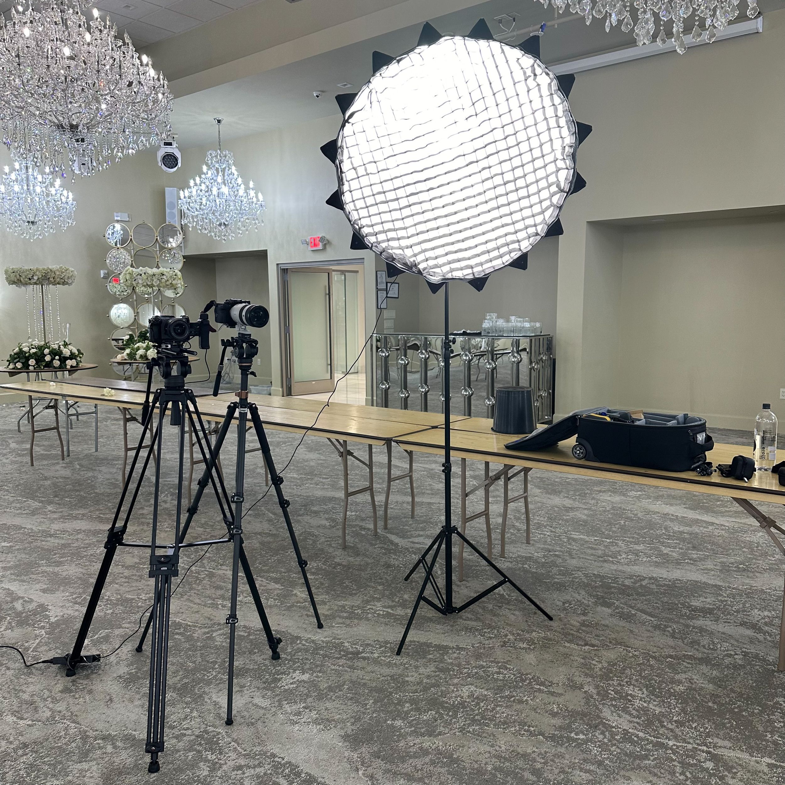 Professional studio setup with lighting equipment, tripods, and crystal chandeliers in a spacious indoor location.