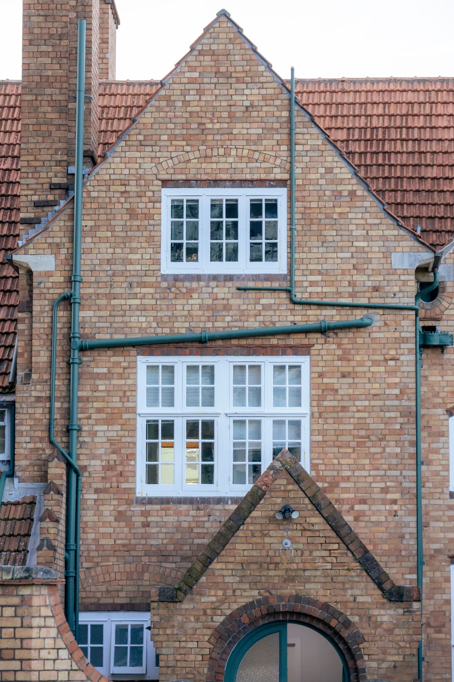 Heritage brick building with red tiled roof and turquoise plumbing pipes running across its facade.