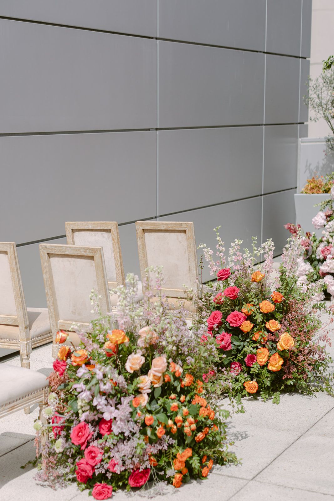Elegant white lace wedding dress photographed against vibrant floral arch installation on urban rooftop terrace.