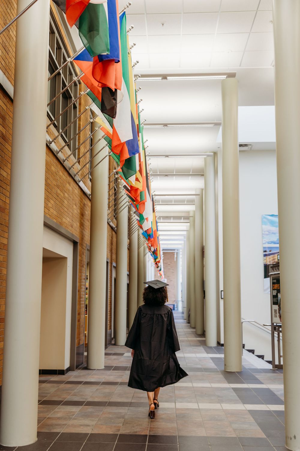 A graduate walks down a hallway decorated with colorful flags and columns.