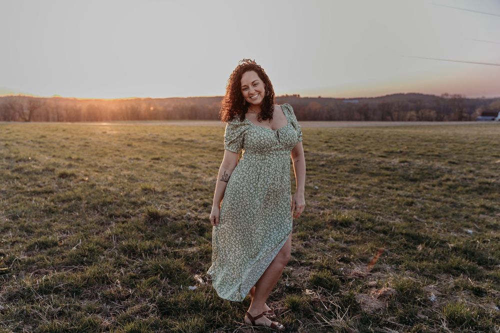 A person in a floral dress poses in a field during golden hour sunset.