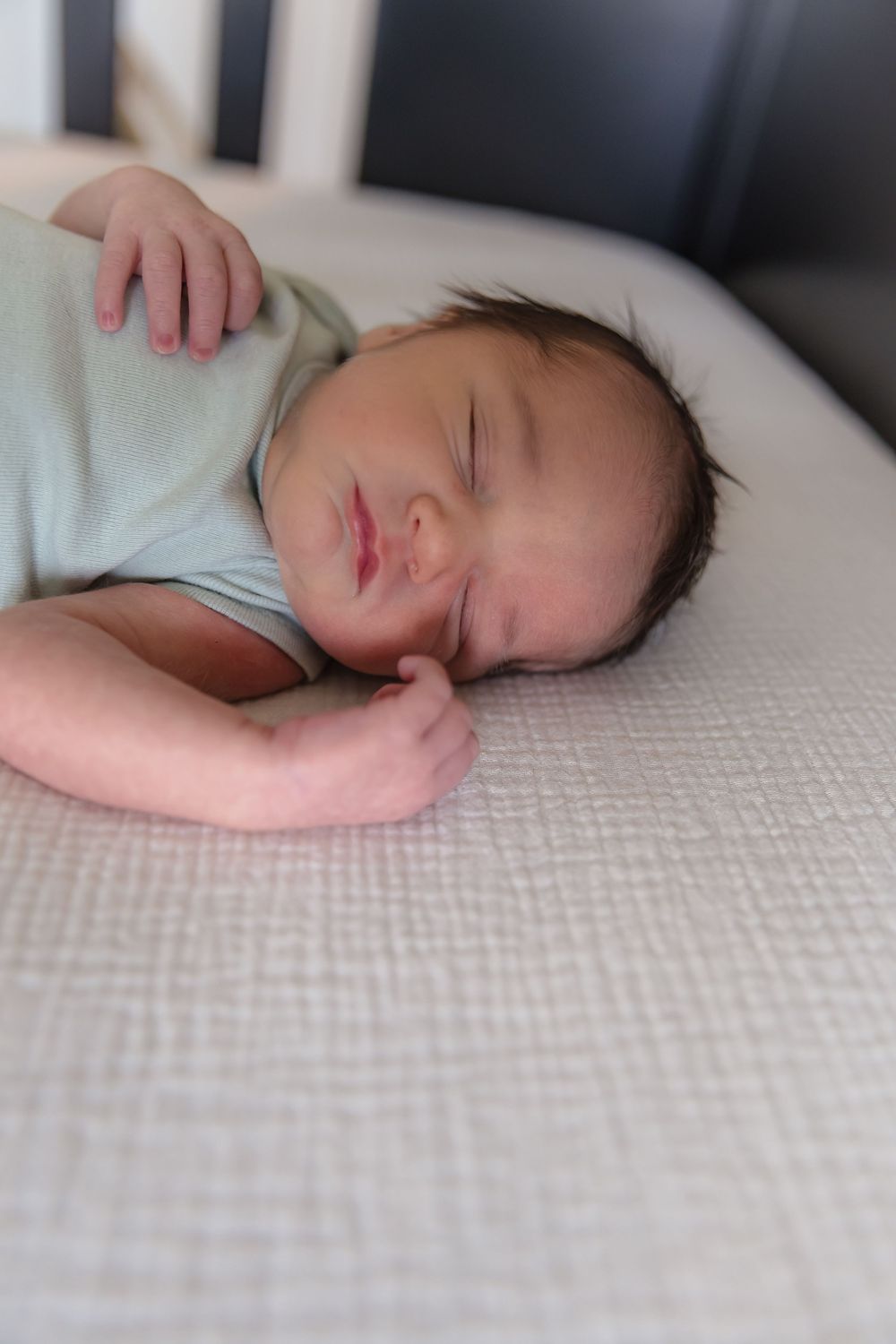 A peaceful sleeping baby in light clothing rests on textured white bedding.