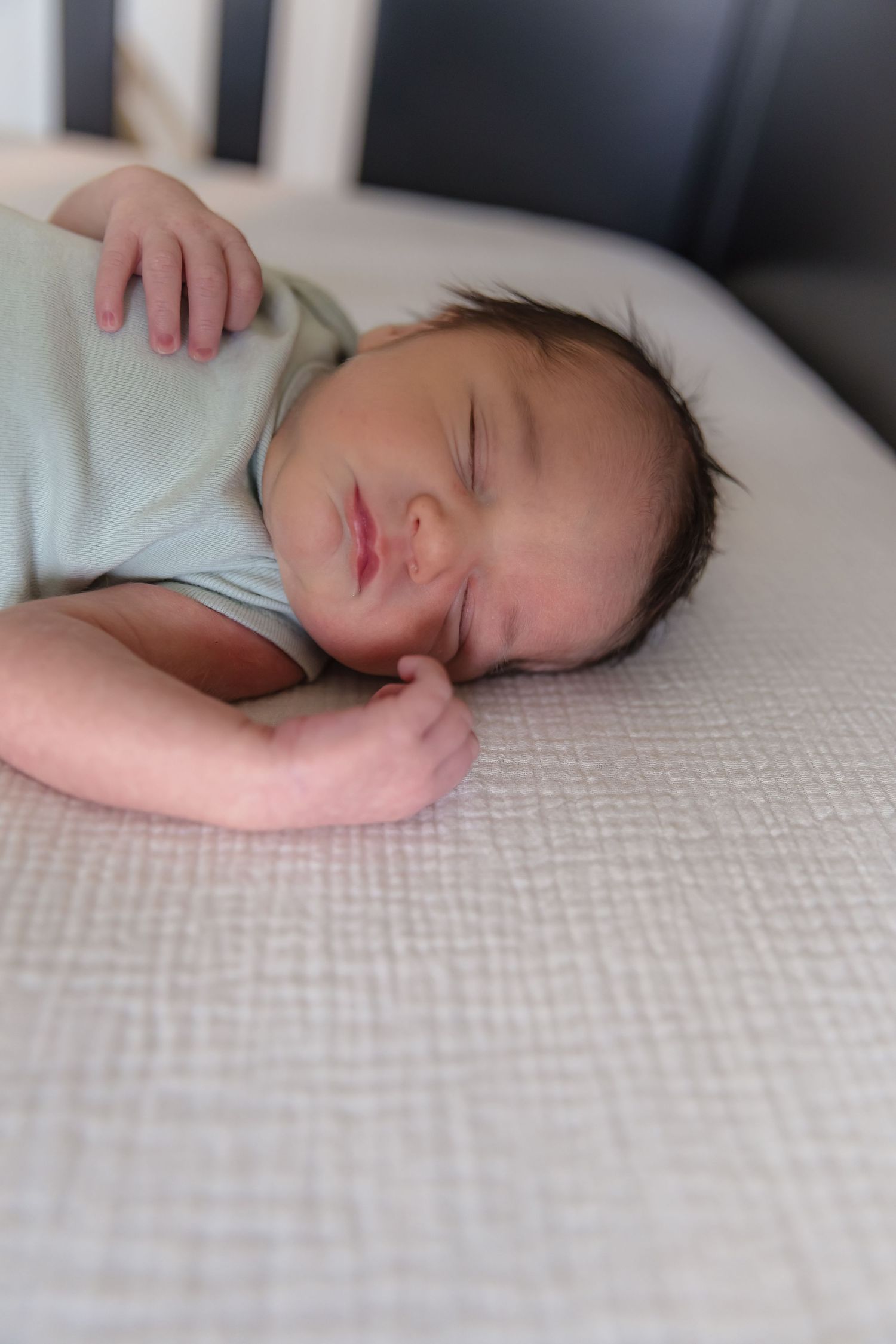 A peaceful sleeping baby in light clothing rests on textured white bedding.