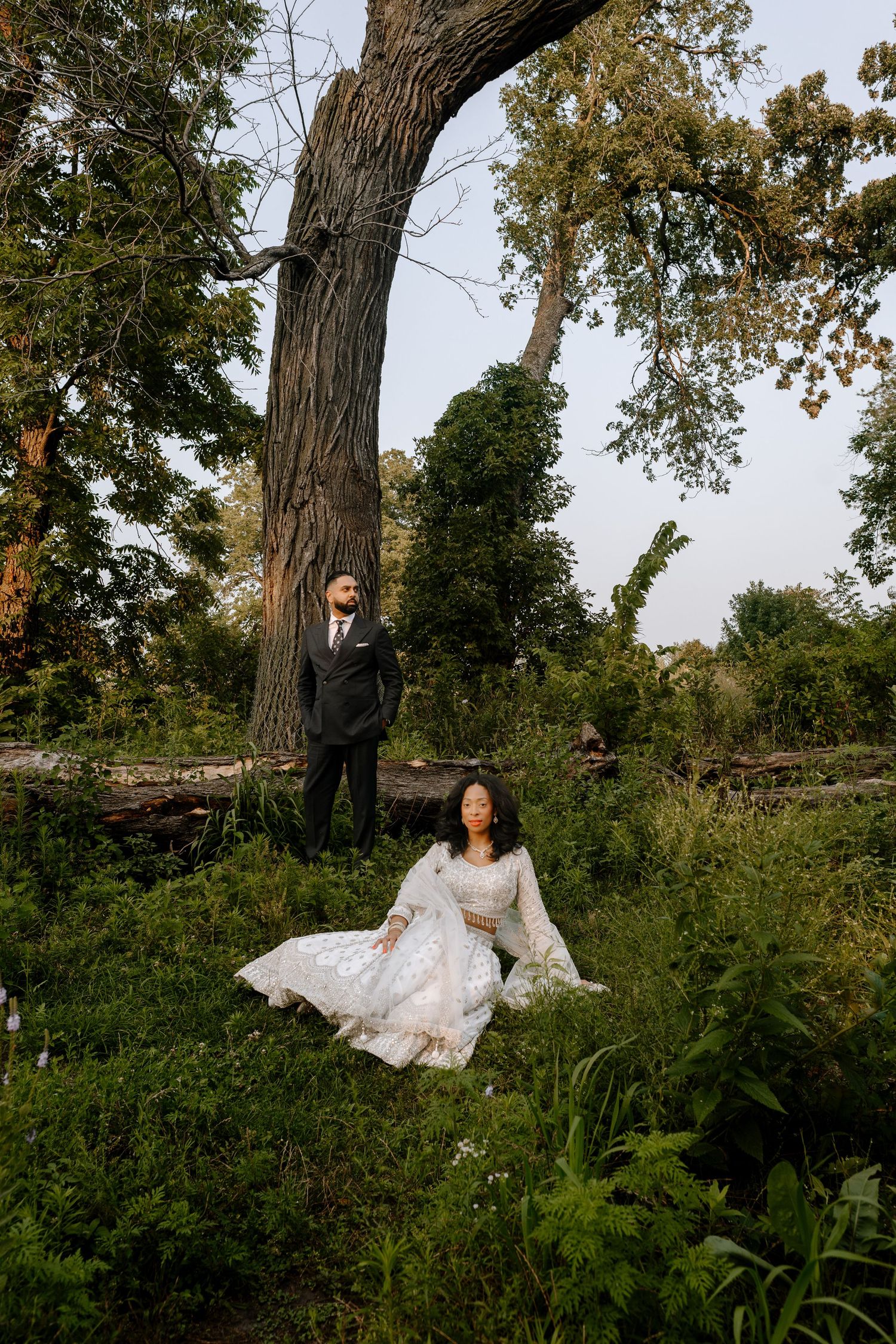 A couple poses amid lush greenery and a large tree trunk during a romantic outdoor photo session in nature.