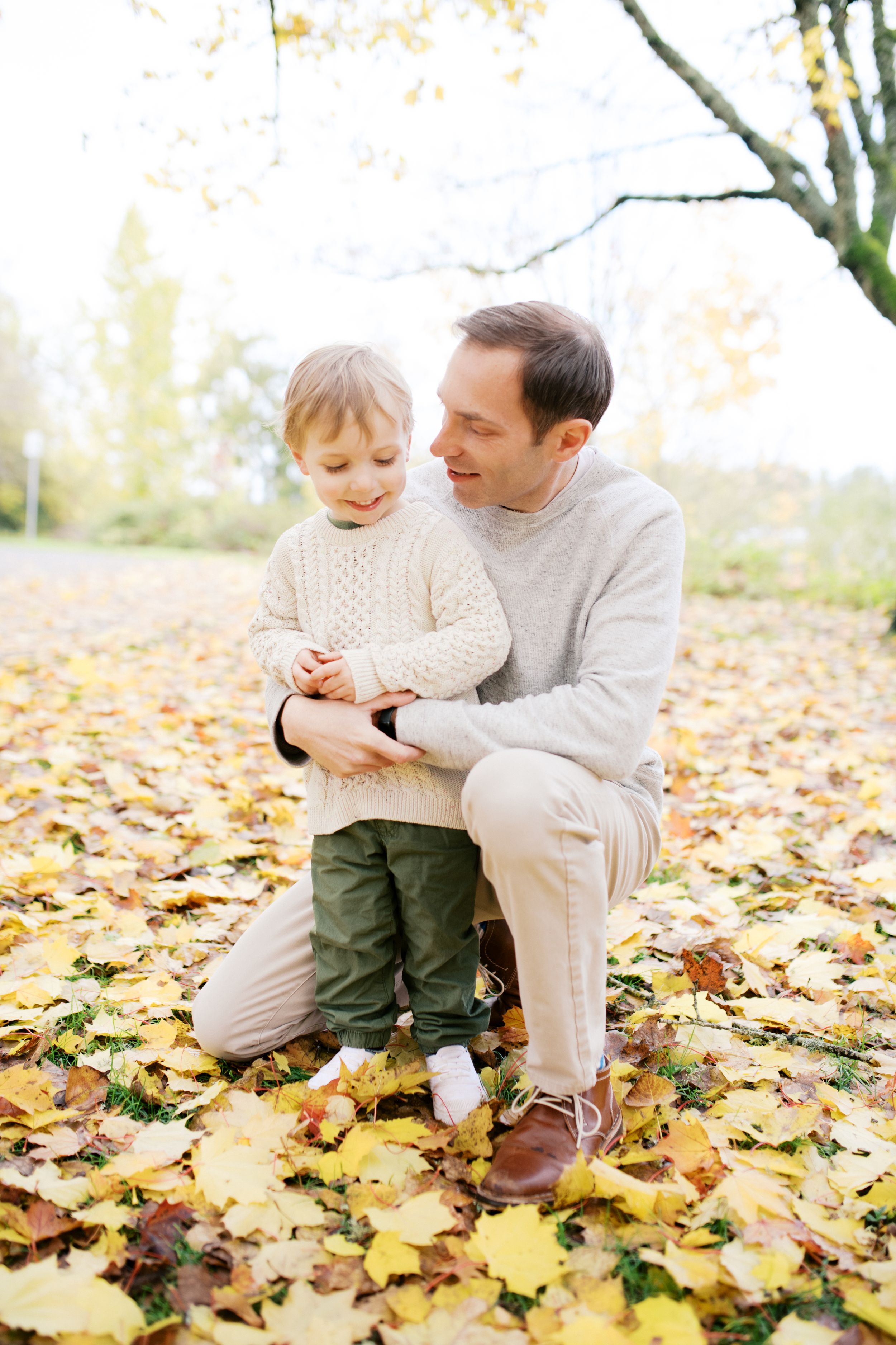 Pair spending time together outdoors on fallen autumn leaves wearing coordinating cream colored sweaters.