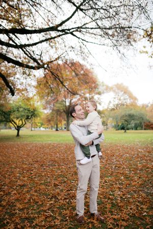 A couple shares an intimate autumn moment in a park covered with fallen orange and brown leaves.