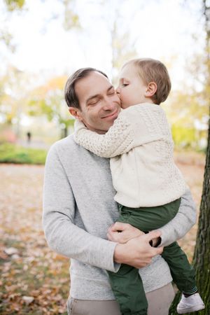 A tender moment shared between a parent and child outdoors among autumn leaves on a bright fall day.