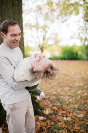 A couple in white winter outfits share playful moments together in a park filled with fallen autumn leaves.