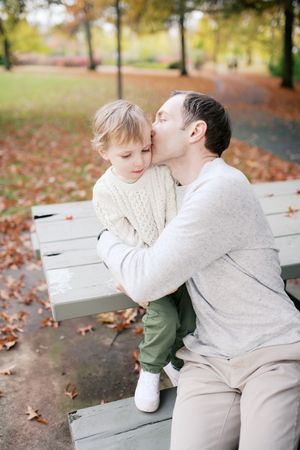 A tender moment shared between parent and child on a park bench surrounded by autumn leaves.